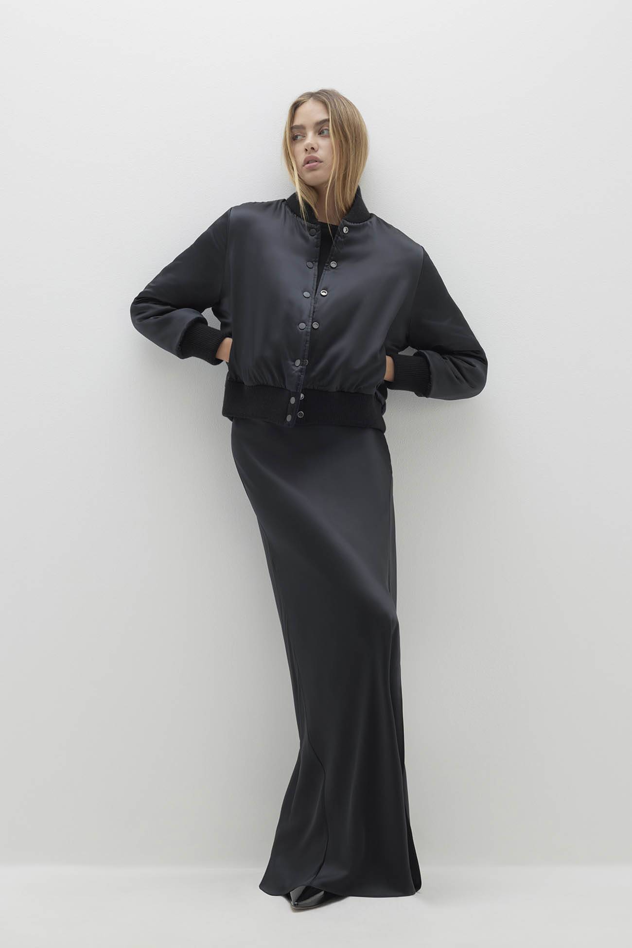 Model wearing stylish outerwear, featuring a cropped black bomber jacket and a long sleek dress.