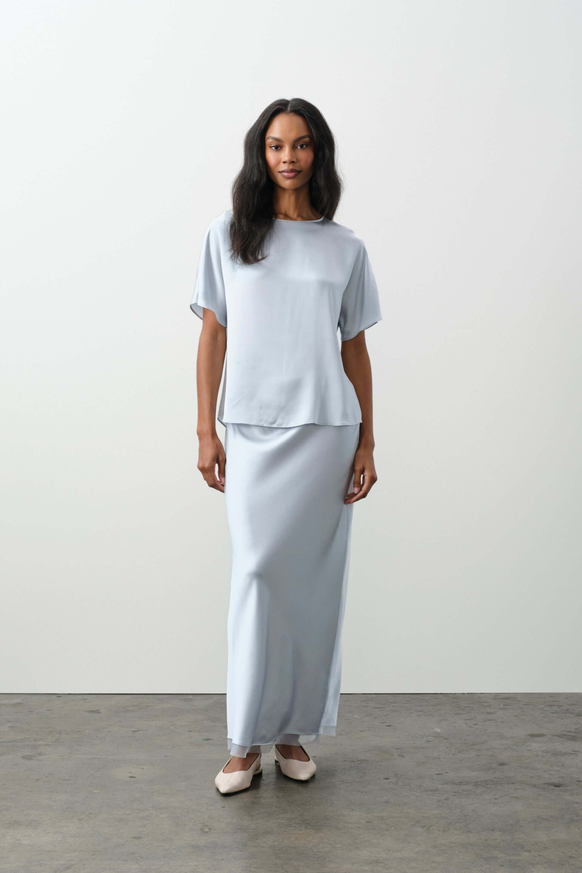 Model wearing light blue outfit from the Bottoms collection, featuring a flowy top and maxi skirt.